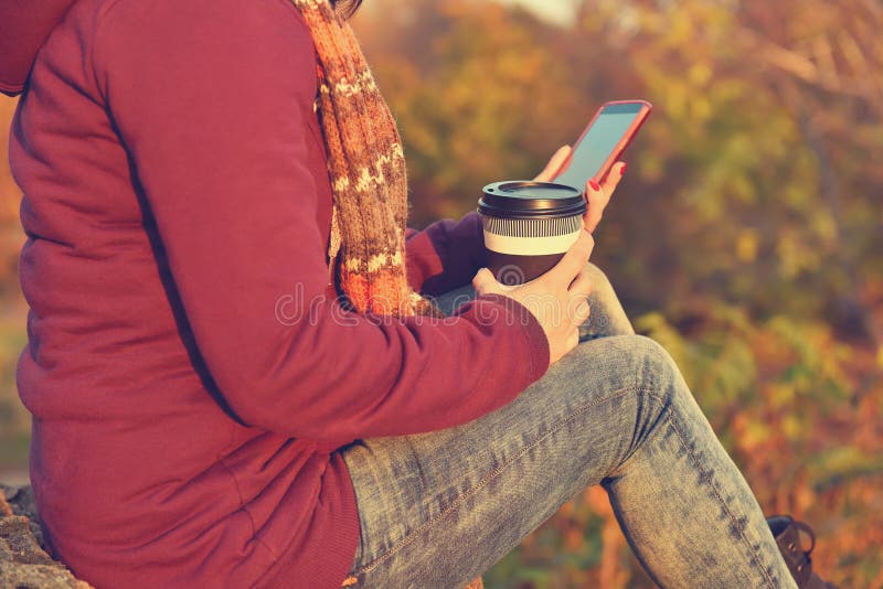 Ragazza dei pantaloni a vita bassa che tiene tazza di caffè e telefono fotografie stock Ragazza dei pantaloni a vita bassa che tiene tazza di caffè e telefono fotografie stock