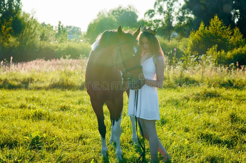 Ragazza dell'adolescente in vestito bianco con il cavallo nel campo fotografia stock libera da diritti Ragazza dell'adolescente in vestito bianco con il cavallo nel campo fotografia stock libera da diritti