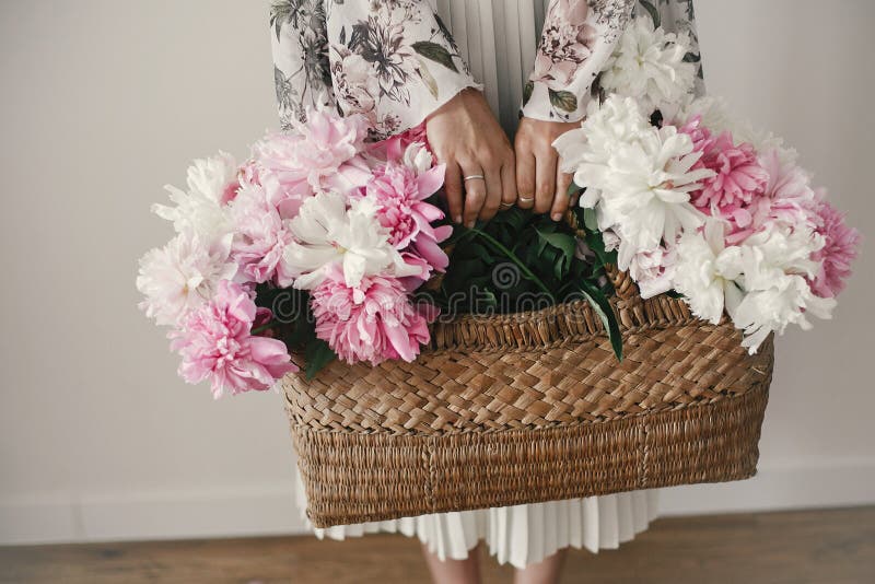 Ragazza di Boho che tiene le peonie bianche e di rosa in canestro rustico Donna alla moda dei pantaloni a vita bassa in fiori del fotografie stock libere da diritti Ragazza di Boho che tiene le peonie bianche e di rosa in canestro rustico Donna alla moda dei pantaloni a vita bassa in fiori del fotografie stock libere da diritti