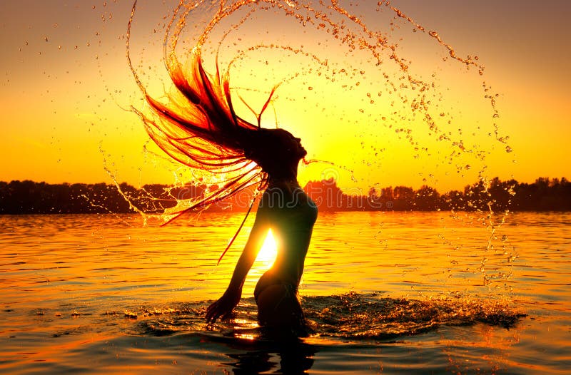 Ragazza di modello di bellezza che spruzza acqua con i suoi capelli Siluetta della ragazza sopra il cielo di tramonto Nuotando e