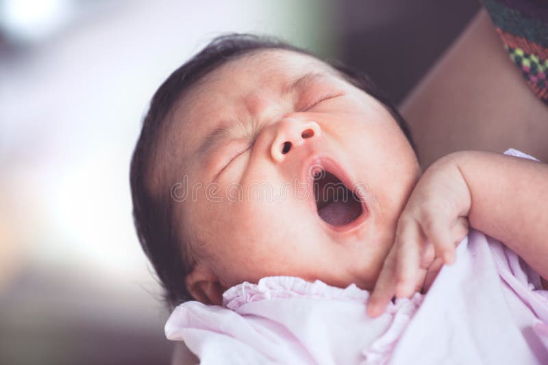 Ragazza di neonato asiatica sveglia che dorme e che sbadiglia sul braccio del ` s della madre fotografia stock Ragazza di neonato asiatica sveglia che dorme e che sbadiglia sul braccio del ` s della madre fotografia stock