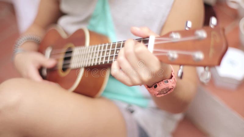 Ragazza di seduta in breve che giocano la chitarra delle ukulele sulla via Giorno pieno di sole di estate Musica stringhe Suono