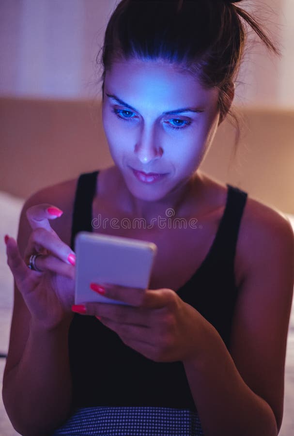 Addicted girl looking at mobile phone in the dimmed bedroom. Addicted girl looking at mobile phone in the dimmed bedroom