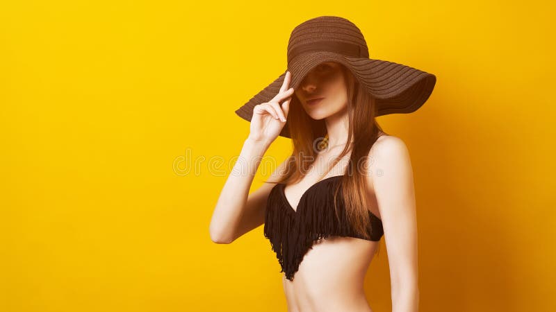Ragazza in estate black hat e costume da bagno Concetto nero di venerdì Giovane donna sensuale in swimwear, isolato sopra giallo fotografia stock Ragazza in estate black hat e costume da bagno Concetto nero di venerdì Giovane donna sensuale in swimwear, isolato sopra giallo fotografia stock