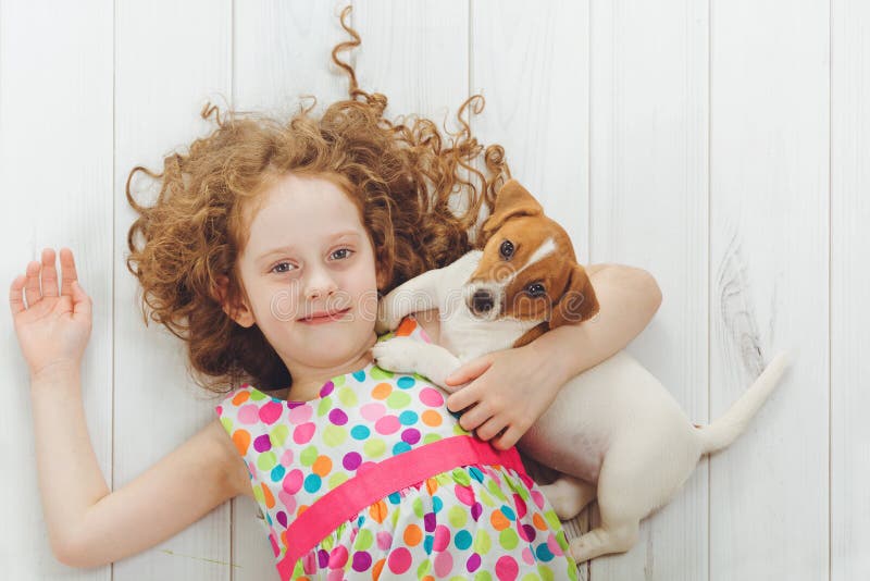 Ragazza felice con il suo terrier di Jack russell del cucciolo che si trova su un di legno fotografia stock libera da diritti Ragazza felice con il suo terrier di Jack russell del cucciolo che si trova su un di legno fotografia stock libera da diritti