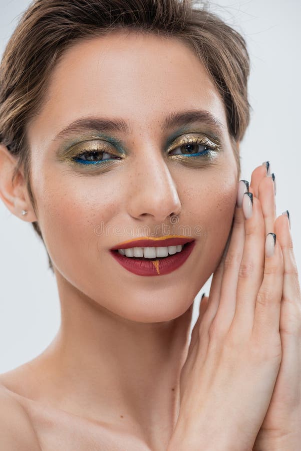 Ragazza felice con occhio scintillante. Giovane donna felice con un trucco degli occhi scintillante e i capelli corti in piedi, con le mani pregate sull'immagine grigia
