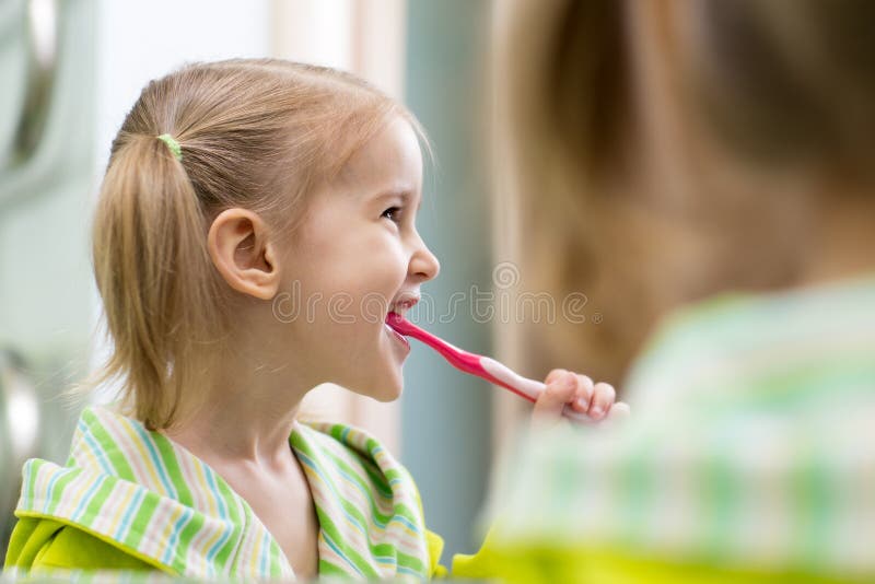 Ragazza felice del bambino che esamina specchio facendo uso dei denti di pulizia dello spazzolino da denti in bagno ogni mattina fotografia stock libera da diritti Ragazza felice del bambino che esamina specchio facendo uso dei denti di pulizia dello spazzolino da denti in bagno ogni mattina fotografia stock libera da diritti