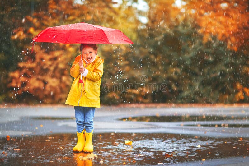 Ragazza felice del bambino con un ombrello e gli stivali di gomma in pozza sopra immagini stock