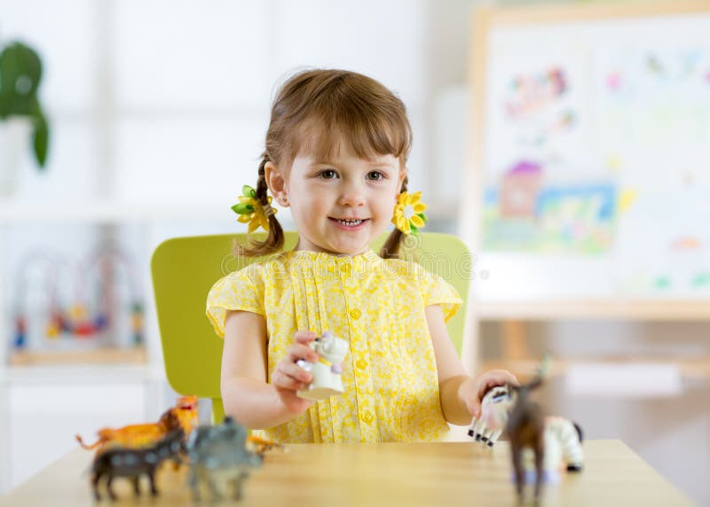 Ragazza felice del bambino Il bambino sorridente del bambino gioca i giocattoli animali a casa o la scuola materna fotografia stock