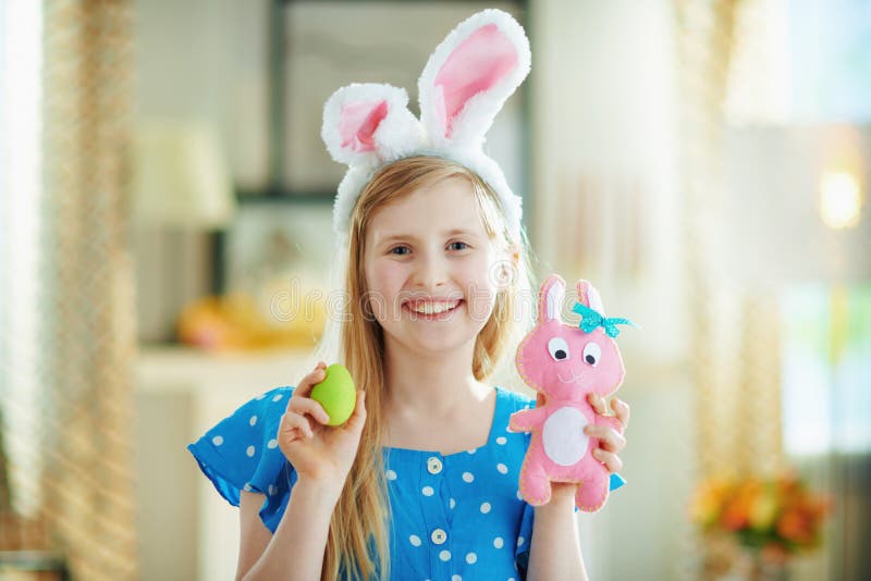 Ragazza felice e moderna che mostra un giocattolo di coniglio rosa e un uovo di Pasqua verde