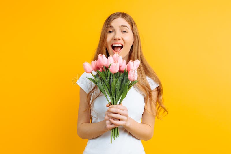 Ragazza felice, tenente un mazzo dei fiori in sua mano, contentissimo con il regalo su un fondo giallo fotografia stock libera da diritti Ragazza felice, tenente un mazzo dei fiori in sua mano, contentissimo con il regalo su un fondo giallo fotografia stock libera da diritti