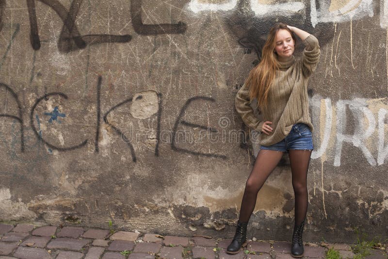 Ragazza graziosa alla moda che posa vicino ad una parete di pietra fotografia stock Ragazza graziosa alla moda che posa vicino ad una parete di pietra fotografia stock