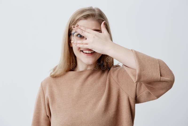 Ragazza graziosa che ha sembrare timido che dà una occhiata tramite le sue dita che dimostrano i suoi denti anche bianchi Giovane fotografia stock Ragazza graziosa che ha sembrare timido che dà una occhiata tramite le sue dita che dimostrano i suoi denti anche bianchi Giovane fotografia stock
