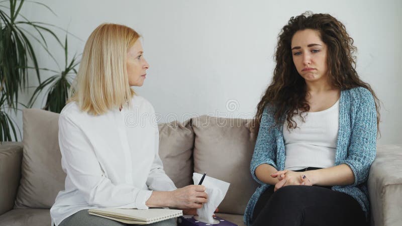 Ragazza gridante turbata che ha consultazione con lo psicologo femminile professionista in cui che dà tessuto di carta alla donna