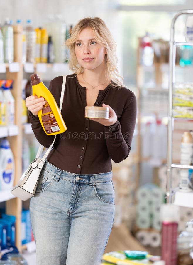 Ragazza interessata concentrata sceglie attentamente parquet e detersivo per legno nel reparto hardware del supermercato fotografia stock