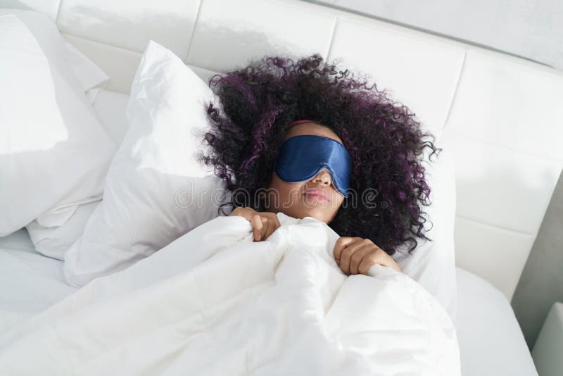 Ragazza nera stanca che sveglia a letto con la maschera di sonno fotografia stock libera da diritti Ragazza nera stanca che sveglia a letto con la maschera di sonno fotografia stock libera da diritti