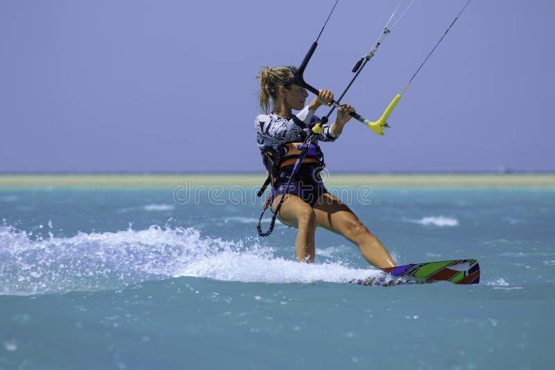 Kite surfing girl in sexy swimsuit with kite in sky on board in blue sea riding waves with water splash. Recreational activity, water sports, action, hobby and fun in summer time. Kiteboarding sport. Kite surfing girl in sexy swimsuit with kite in sky on board in blue sea riding waves with water splash. Recreational activity, water sports, action, hobby and fun in summer time. Kiteboarding sport