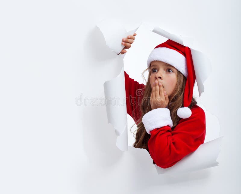 Ragazza sorpresa di Santa che guarda attraverso il foro in carta fotografie stock libere da diritti Ragazza sorpresa di Santa che guarda attraverso il foro in carta fotografie stock libere da diritti
