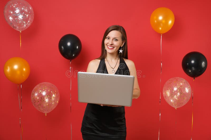 Ragazza sorridente in poco vestito nero che lavora al computer del pc del computer portatile mentre celebrando sugli aerostati ro fotografia stock Ragazza sorridente in poco vestito nero che lavora al computer del pc del computer portatile mentre celebrando sugli aerostati ro fotografia stock