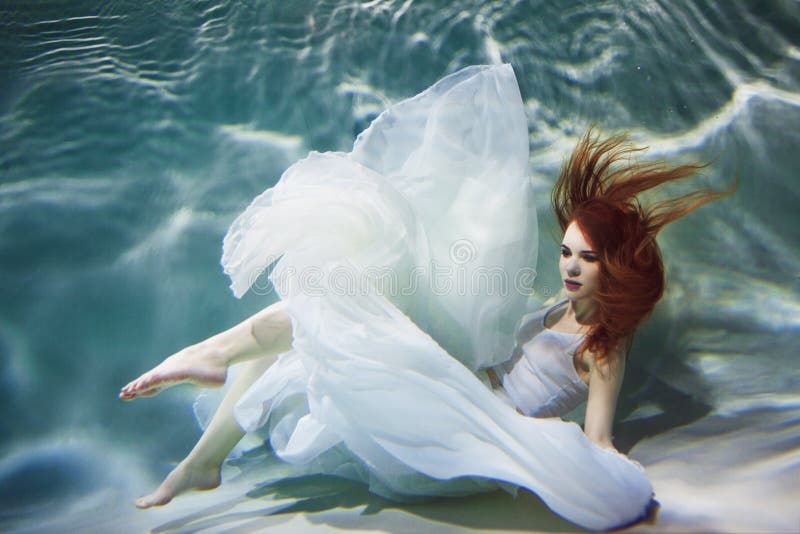 Ragazza subacquea Bella donna dai capelli rossi in un vestito bianco, nuotante sotto l'acqua fotografie stock libere da diritti Ragazza subacquea Bella donna dai capelli rossi in un vestito bianco, nuotante sotto l'acqua fotografie stock libere da diritti