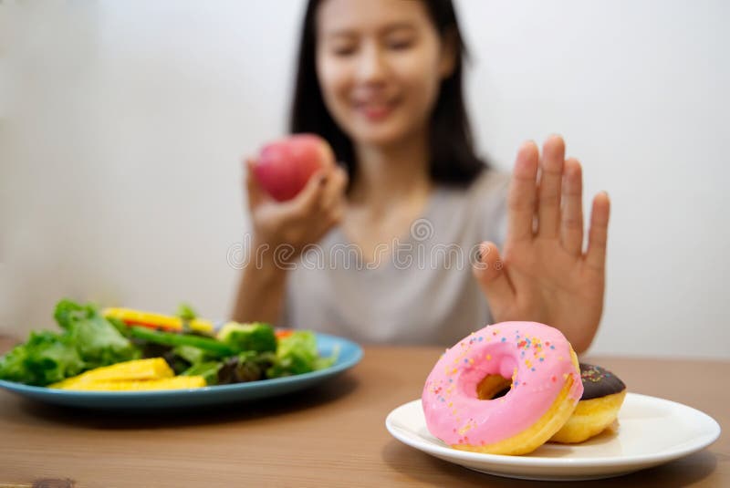 Close up female using hand reject junk food by pushing out her favorite donuts and choose red apple and salad for good health. Close up female using hand reject junk food by pushing out her favorite donuts and choose red apple and salad for good health