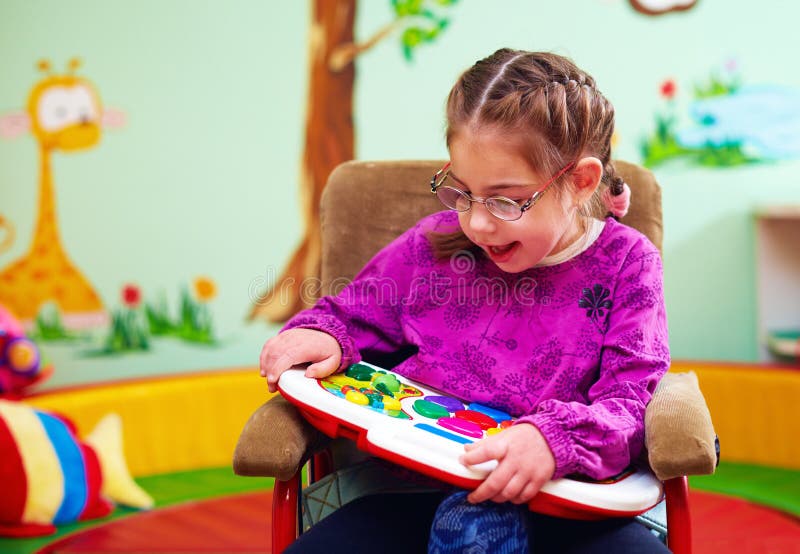 Ragazza sveglia in sedia a rotelle che gioca con il giocattolo di sviluppo nell'asilo per i bambini con i bisogni speciali