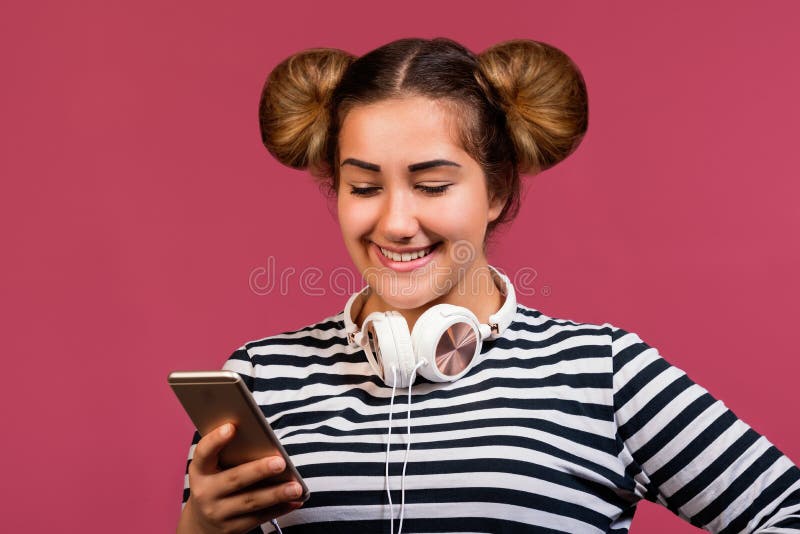 Ragazza teenager con il telefono divertente di uso dell'acconciatura da ascoltare la musica su fondo rosa fotografia stock Ragazza teenager con il telefono divertente di uso dell'acconciatura da ascoltare la musica su fondo rosa fotografia stock