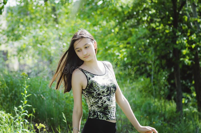 Ragazza teenager graziosa castana con capelli lunghi su un fondo della natura di estate fotografia stock Ragazza teenager graziosa castana con capelli lunghi su un fondo della natura di estate fotografia stock