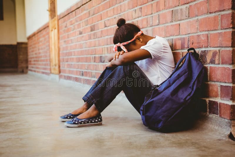 Ragazza tesa che si siede contro il muro di mattoni in corridoio della scuola immagine stock libera da diritti Ragazza tesa che si siede contro il muro di mattoni in corridoio della scuola immagine stock libera da diritti