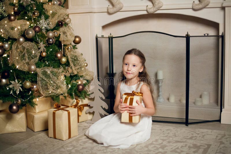 Ragazza in vestito che si siede vicino all'albero di Natale e che tiene i regali immagini stock libere da diritti Ragazza in vestito che si siede vicino all'albero di Natale e che tiene i regali immagini stock libere da diritti