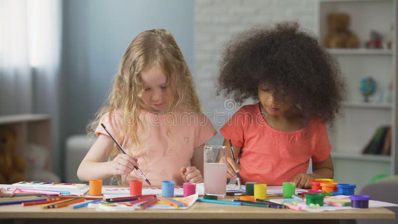 Ragazze caucasiche e afroamericane attente che dipingono alla scuola di arte, tempo libero