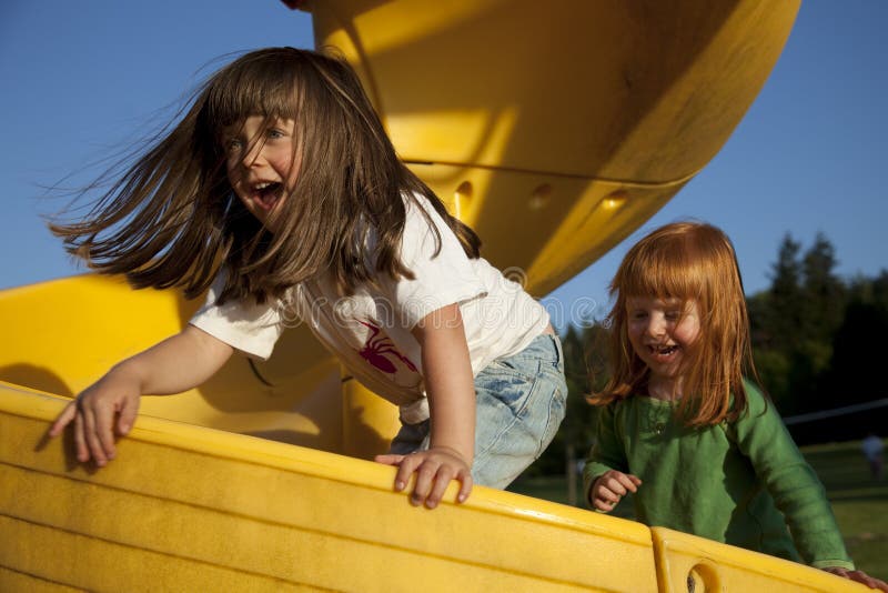 Two smiling girls playing on yellow slide. Horizontal. Two smiling girls playing on yellow slide. Horizontal.