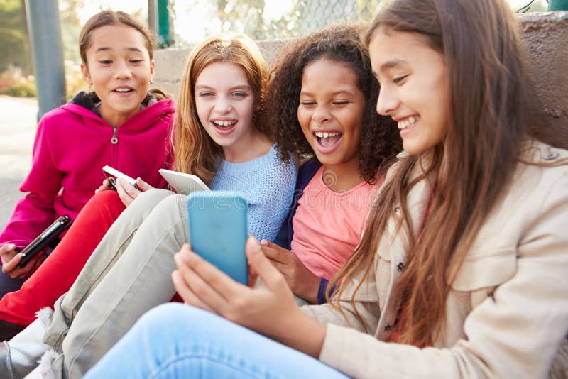 Ragazze che utilizzano le compresse ed i telefoni cellulari di Digital nel parco fotografie stock libere da diritti Ragazze che utilizzano le compresse ed i telefoni cellulari di Digital nel parco fotografie stock libere da diritti