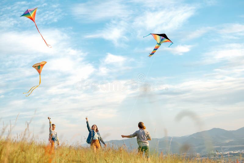 Ragazze sorridenti e fratellino con aquiloni colorati volanti giocattolo all'aperto popolare sul prato della montagna. infanzia fe