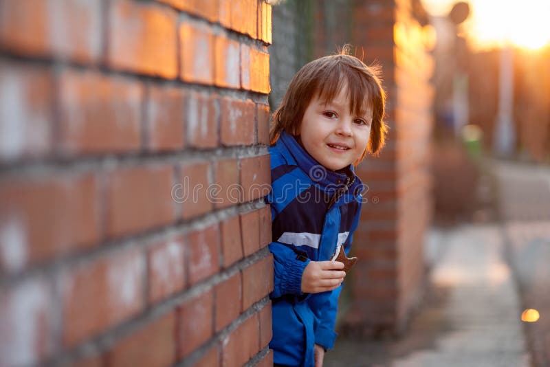 Ragazzino adorabile, accanto al muro di mattoni, mangiante la barra di cioccolato sopra fotografia stock Ragazzino adorabile, accanto al muro di mattoni, mangiante la barra di cioccolato sopra fotografia stock