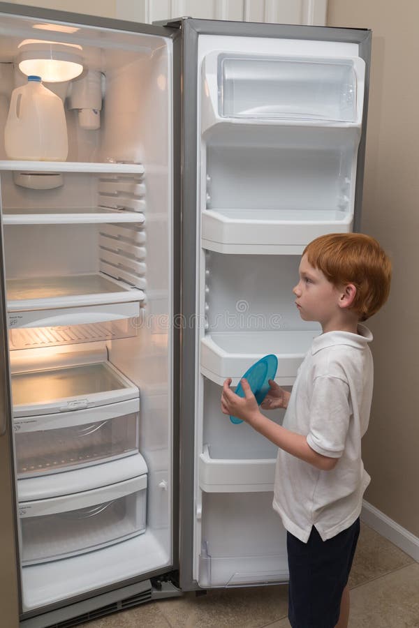 Ragazzino affamato che esamina frigorifero vuoto