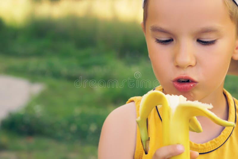Ragazzino che mangia banana, esaminante macchina fotografica con il fronte felice, mostrante i pollici su Il bambino felice gode immagine stock Ragazzino che mangia banana, esaminante macchina fotografica con il fronte felice, mostrante i pollici su Il bambino felice gode immagine stock