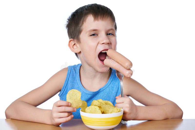 Ragazzino che mangia le salsiccie e le patatine fritte isolate fotografia stock Ragazzino che mangia le salsiccie e le patatine fritte isolate fotografia stock