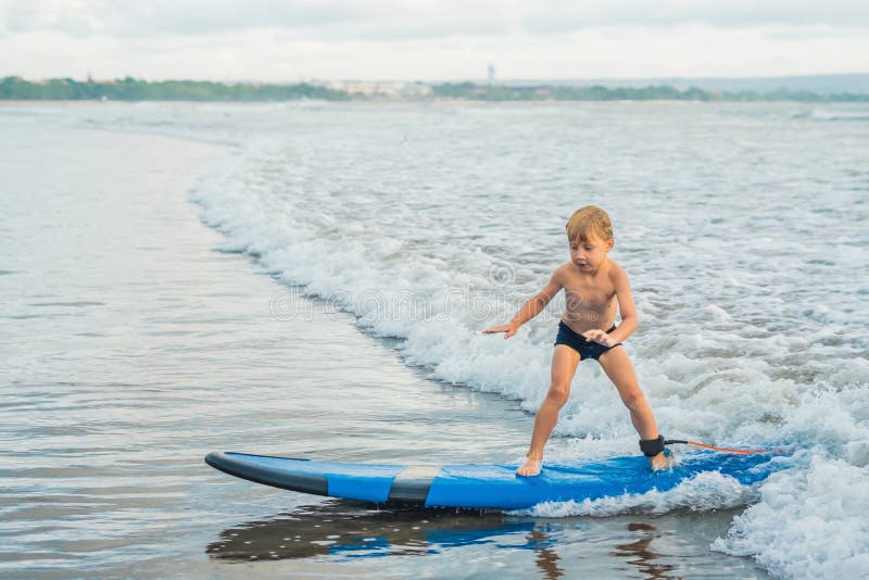 Ragazzino che pratica il surfing sulla spiaggia tropicale Bambino sul bordo di spuma sull'onda di oceano Sport acquatici attivi p fotografia stock libera da diritti Ragazzino che pratica il surfing sulla spiaggia tropicale Bambino sul bordo di spuma sull'onda di oceano Sport acquatici attivi p fotografia stock libera da diritti