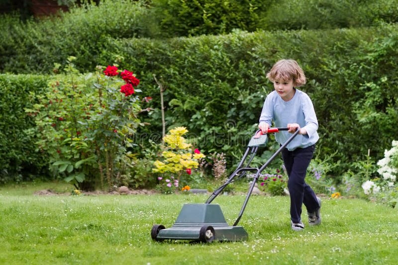 Ragazzino con una falciatrice da giardino nel giardino fotografie stock Ragazzino con una falciatrice da giardino nel giardino fotografie stock