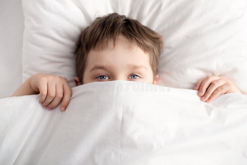 Ragazzino a letto che copre il suo fronte di coperta bianca immagine stock libera da diritti Ragazzino a letto che copre il suo fronte di coperta bianca immagine stock libera da diritti