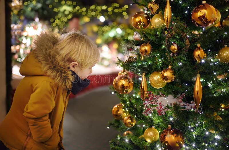 Ragazzino vicino all'albero di Natale che decora le palle dorate all'aperto fotografia stock Ragazzino vicino all'albero di Natale che decora le palle dorate all'aperto fotografia stock
