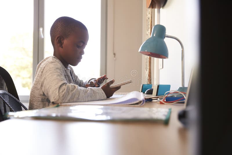 Boy In Bedroom Using Digital Tablet To Do Homework. Boy In Bedroom Using Digital Tablet To Do Homework
