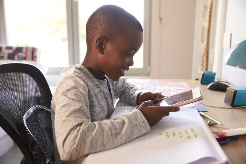 Boy In Bedroom Using Digital Tablet To Do Homework. Boy In Bedroom Using Digital Tablet To Do Homework