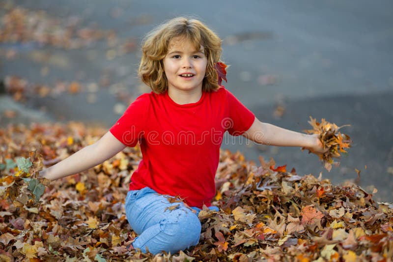 Ragazzo che gioca in una pila di foglie d'autunno. bambino getta foglie d'autunno nel parco d'autunno. divertimento tra bambini. b fotografie stock