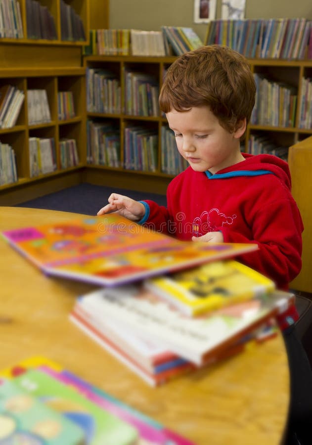 Ragazzo che legge un libro in biblioteca fotografia stock Ragazzo che legge un libro in biblioteca fotografia stock