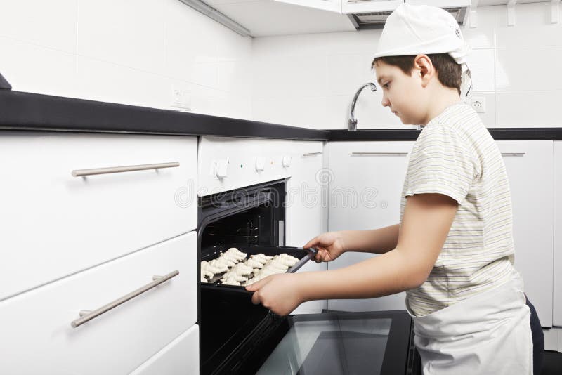 Ragazzo che mette i croissant nel forno fotografia stock Ragazzo che mette i croissant nel forno fotografia stock