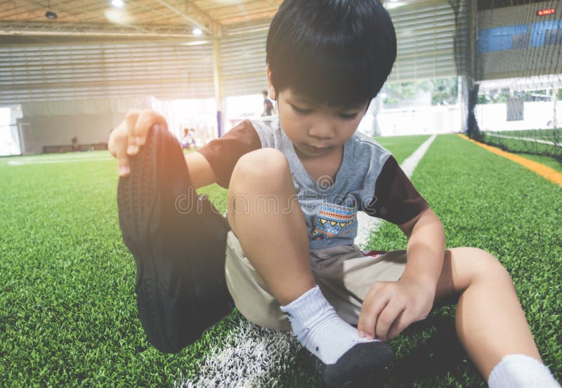 Ragazzo che prende le scarpe fuori da pronto per il terreno di gioco di calcio fotografia stock Ragazzo che prende le scarpe fuori da pronto per il terreno di gioco di calcio fotografia stock