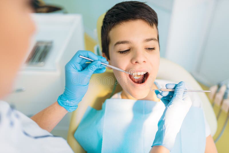 Ragazzo con la bocca aperta in una sedia dentaria immagine stock Ragazzo con la bocca aperta in una sedia dentaria immagine stock