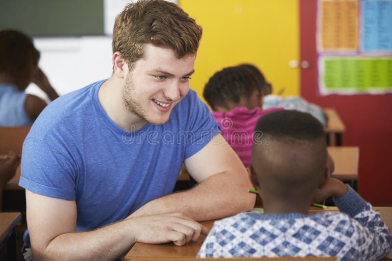 Ragazzo d'aiuto del maschio dell'insegnante bianco del volontario nella classe della scuola elementare fotografia stock Ragazzo d'aiuto del maschio dell'insegnante bianco del volontario nella classe della scuola elementare fotografia stock